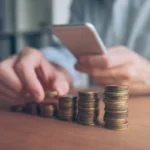 Homme empilant des pièces en consultant son smartphone pour un mini prêt