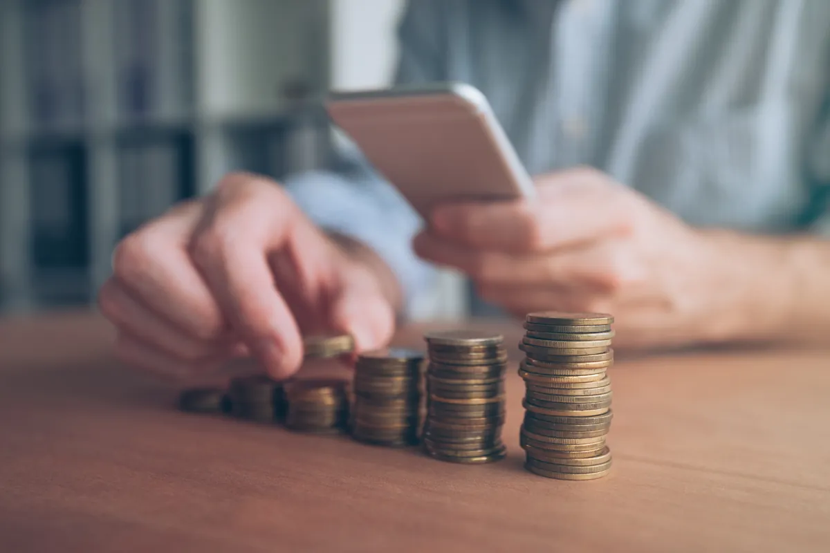 Homme empilant des pièces en consultant son smartphone pour un mini prêt