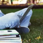 Étudiant révisant sur l'herbe avec ordinateur portable et manuels