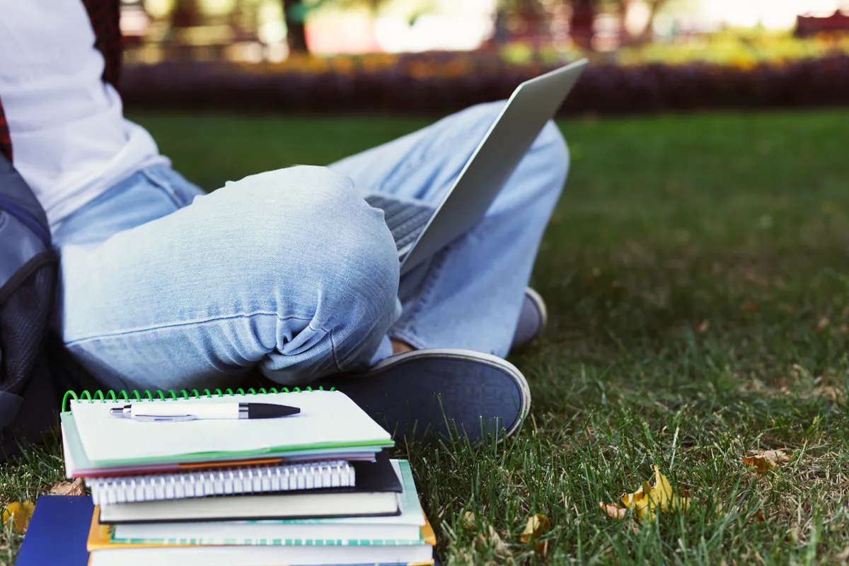 Étudiant révisant sur l'herbe avec ordinateur portable et manuels