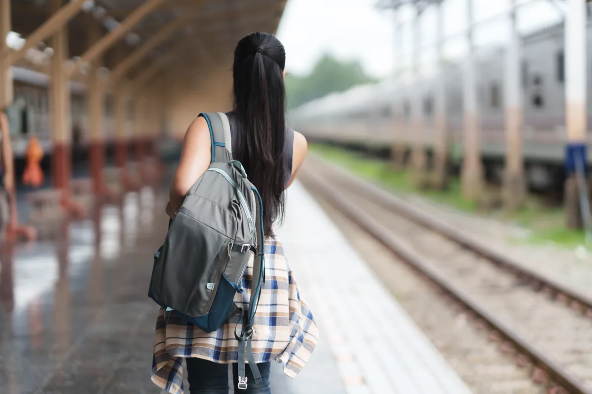 Voyageuse avec sac à dos sur un quai de gare pour un séjour à petit prix