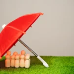 Figurines en bois abritées sous un parapluie rouge, symbole d'assurance