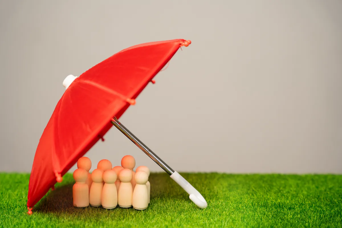 Figurines en bois abritées sous un parapluie rouge, symbole d'assurance
