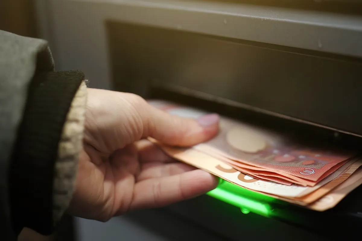 Main retirant des billets en euros à un distributeur automatique