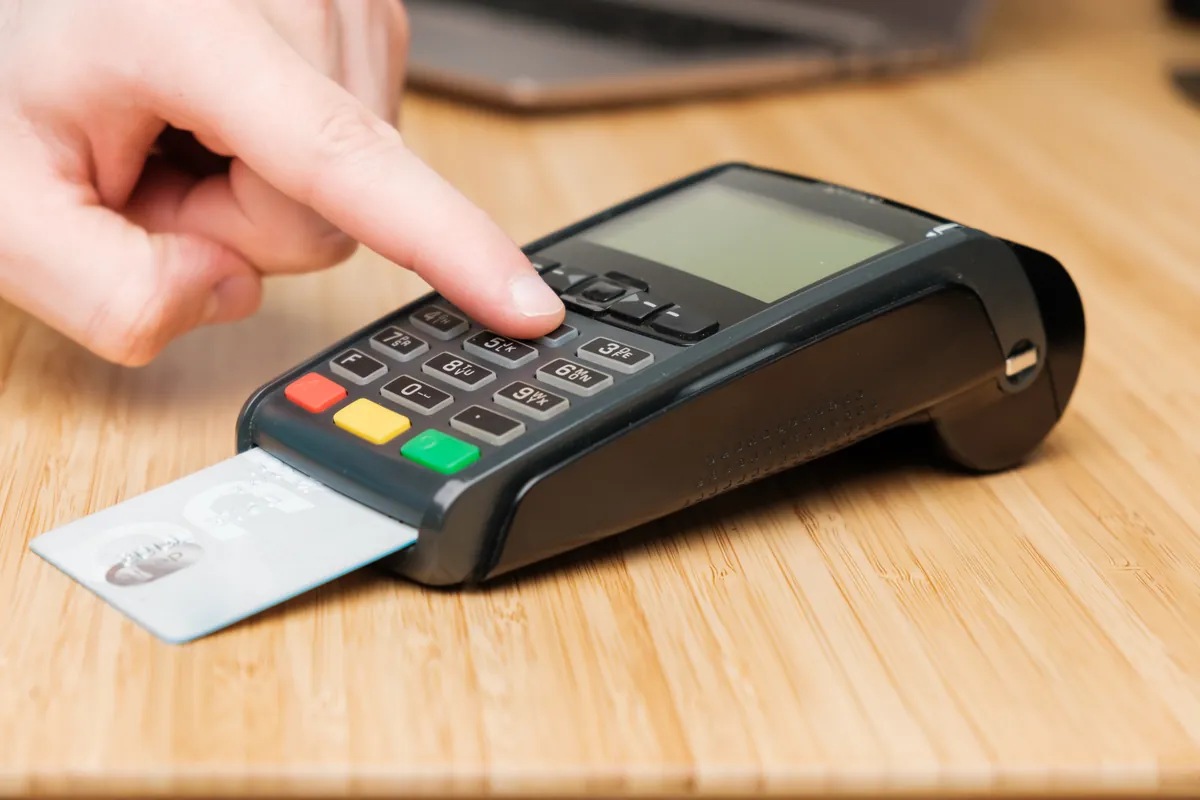 Main tapant son code sur un terminal de paiement avec une carte insérée