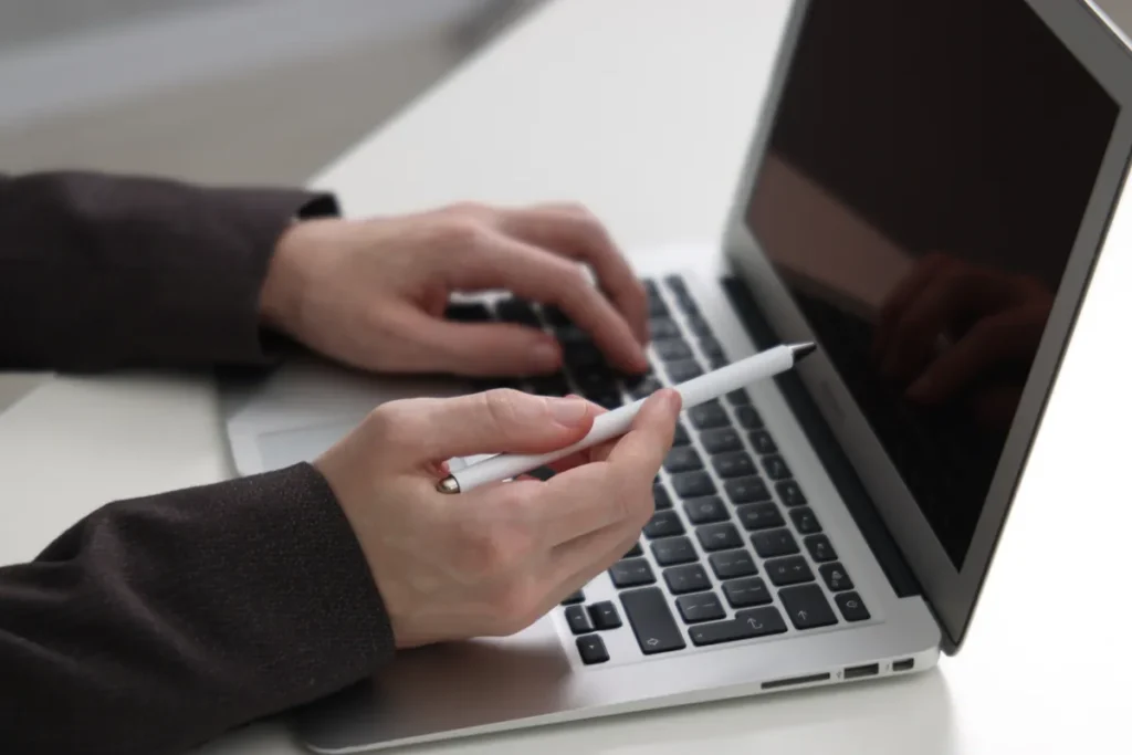 Mains tapant sur un ordinateur portable en tenant un stylo