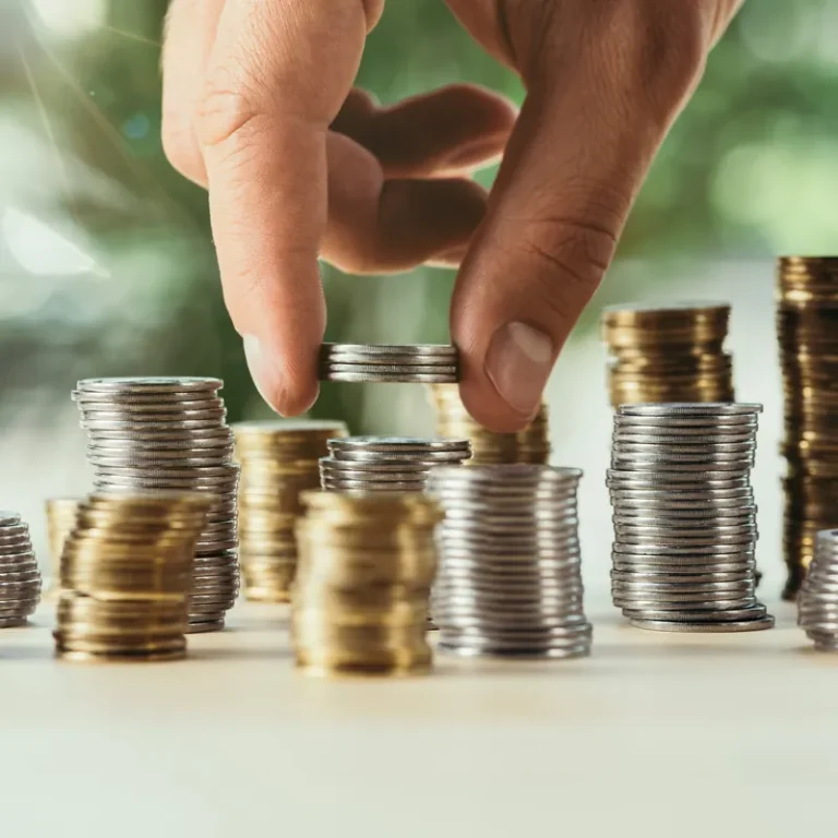 Une main ajoute une pièce sur des piles de pièces de monnaie posées sur une table